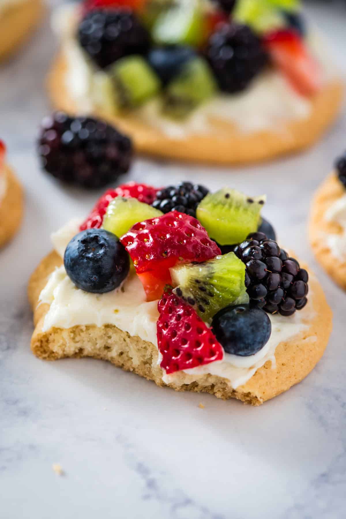 fruit pizza cookie with a bite taken out on a marbled white countertop