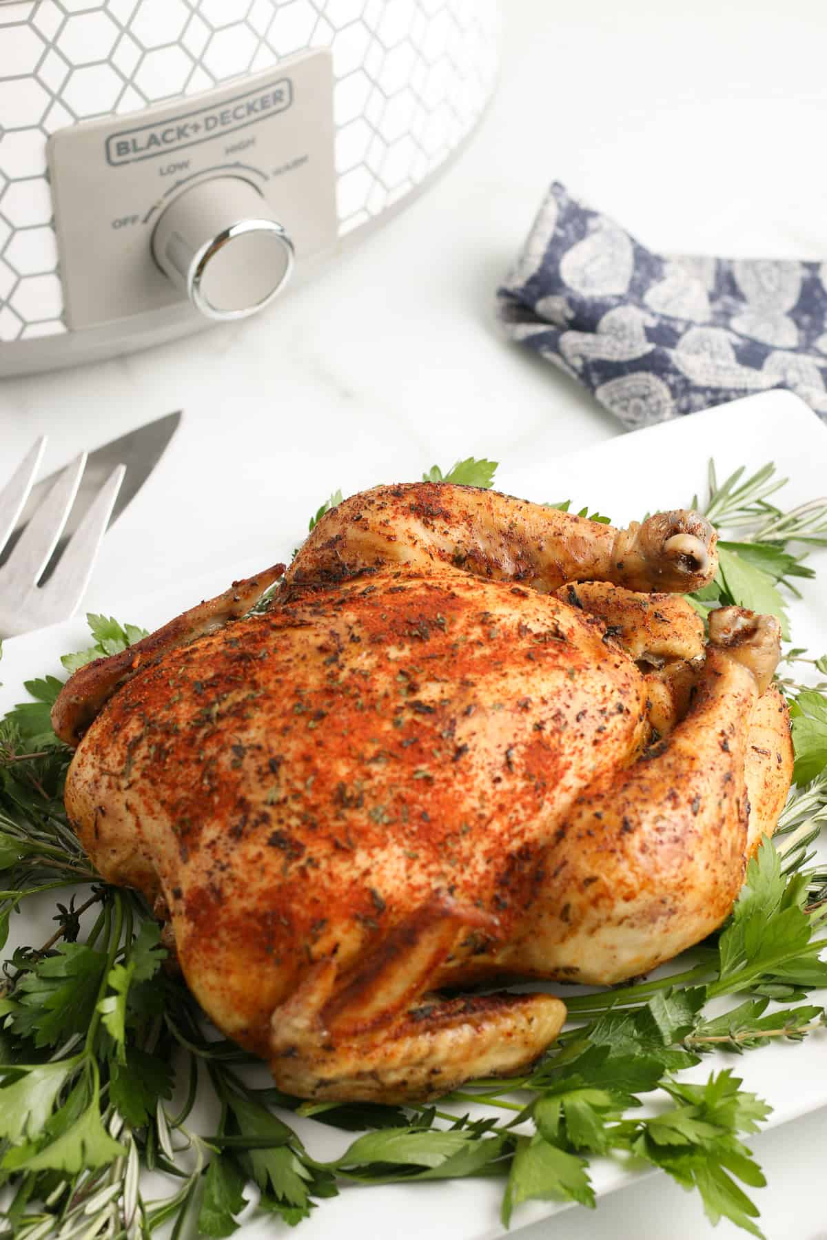 slow cooker whole chicken on a pile of fresh herbs on a white decorative plate