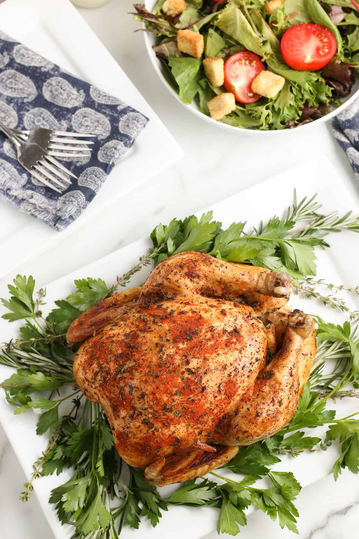crockpot whole chicken on a pile of herbs on a white decorative plate with a small bowl of fresh salad